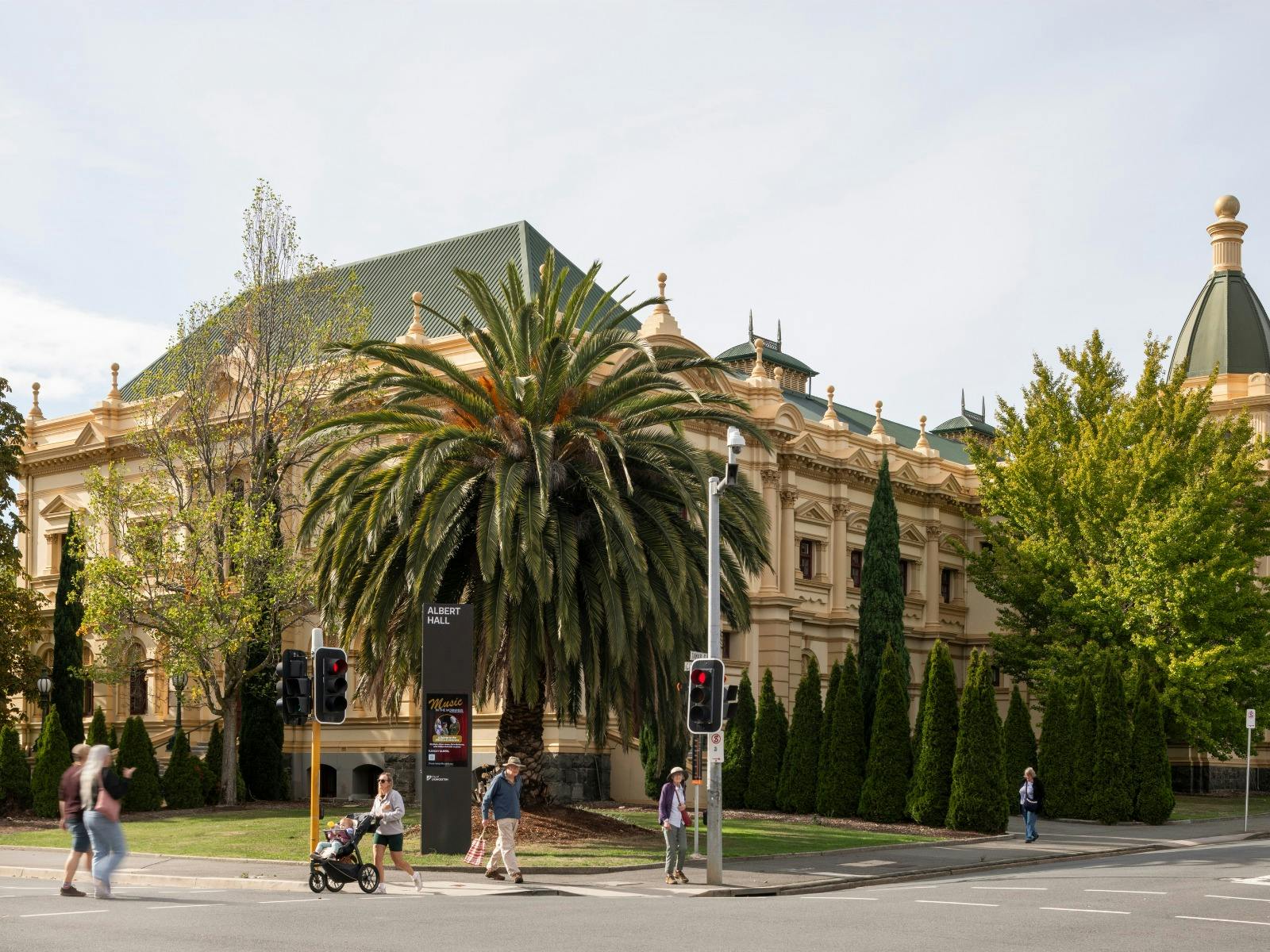 Corner of a city street with a large old building, a palm tree, people crossing the road