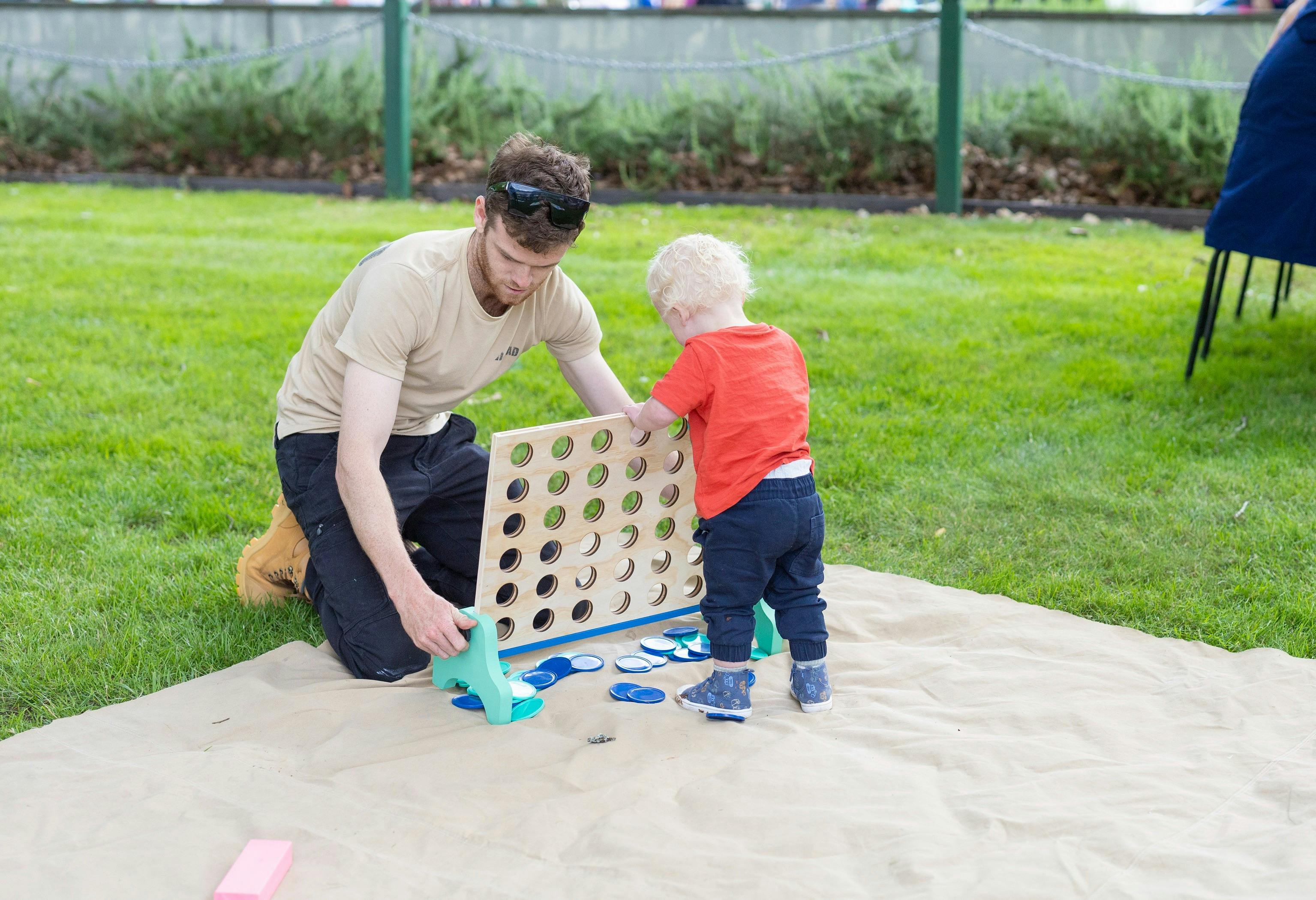 A toddler plays connect 4 with his father.