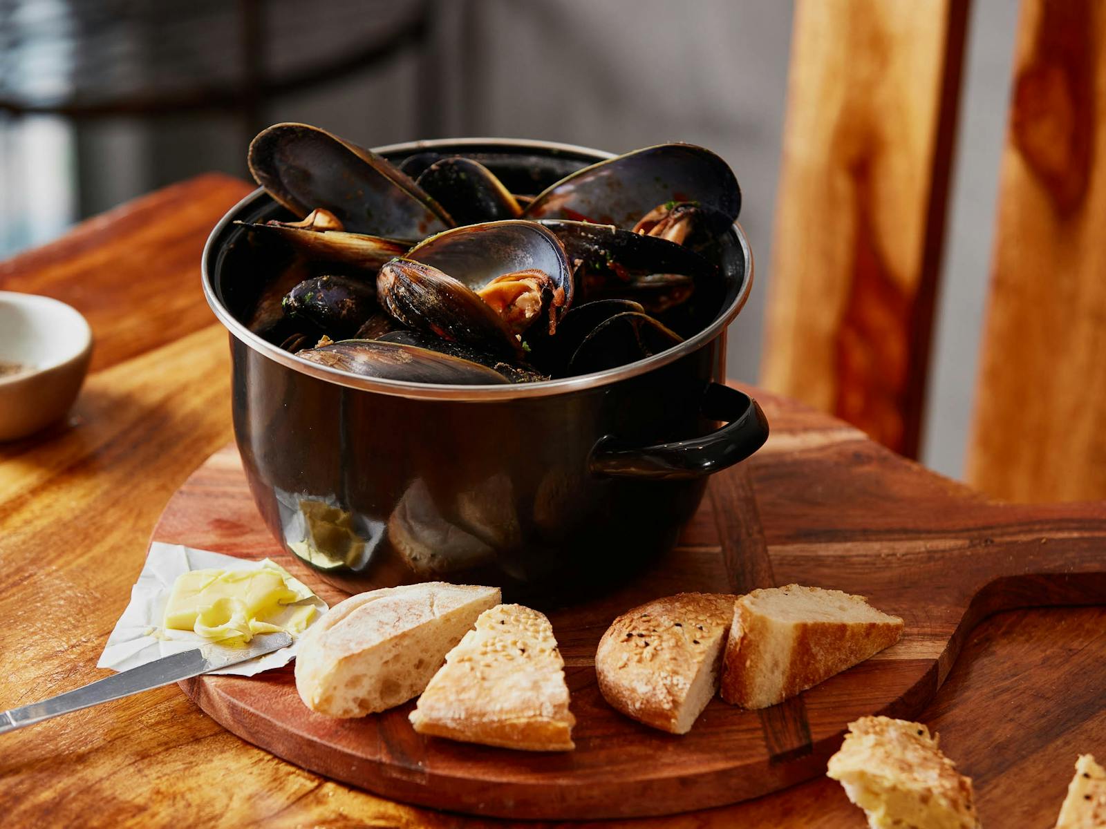 A pot of mussels, covered with a chilli sauce and served with bread slices and butter on the side