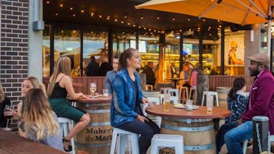 Customers seated outside at a bar with bright orange umbrellas and wooden tables.