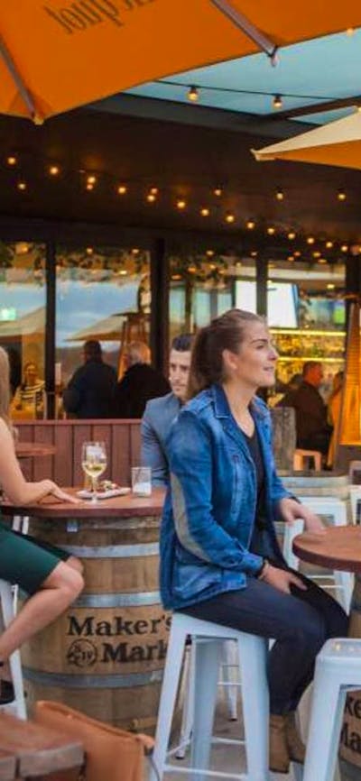 Customers seated outside at a bar with bright orange umbrellas and wooden tables.