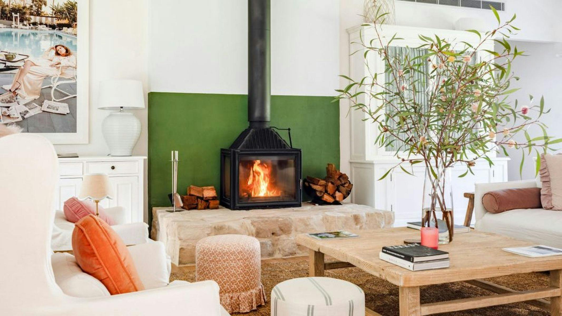 Image of indoor fireplace, fire is lit and blaring. An olive tree sits to the right of room.