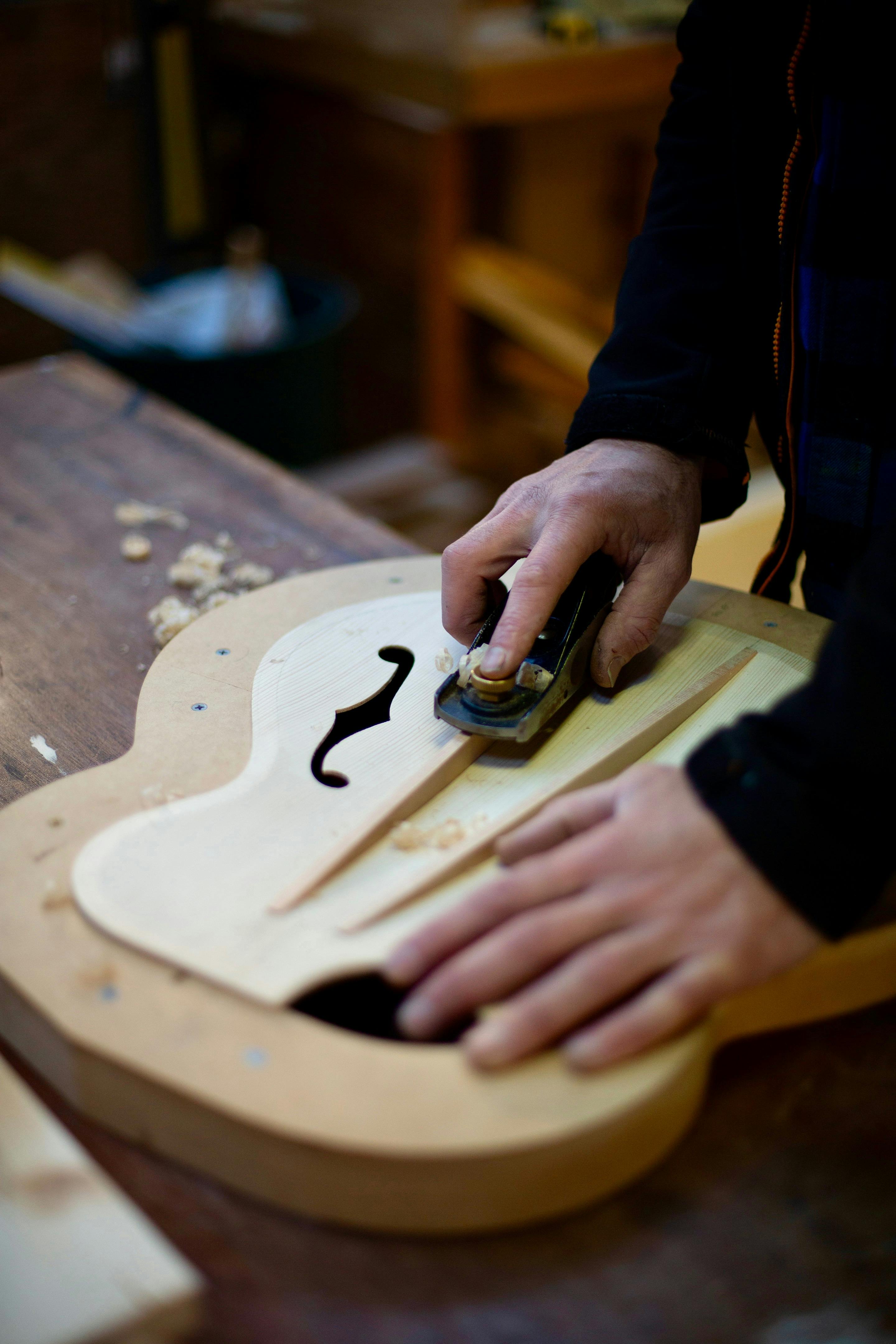 A wooden musical instrument is crafted by hand tools