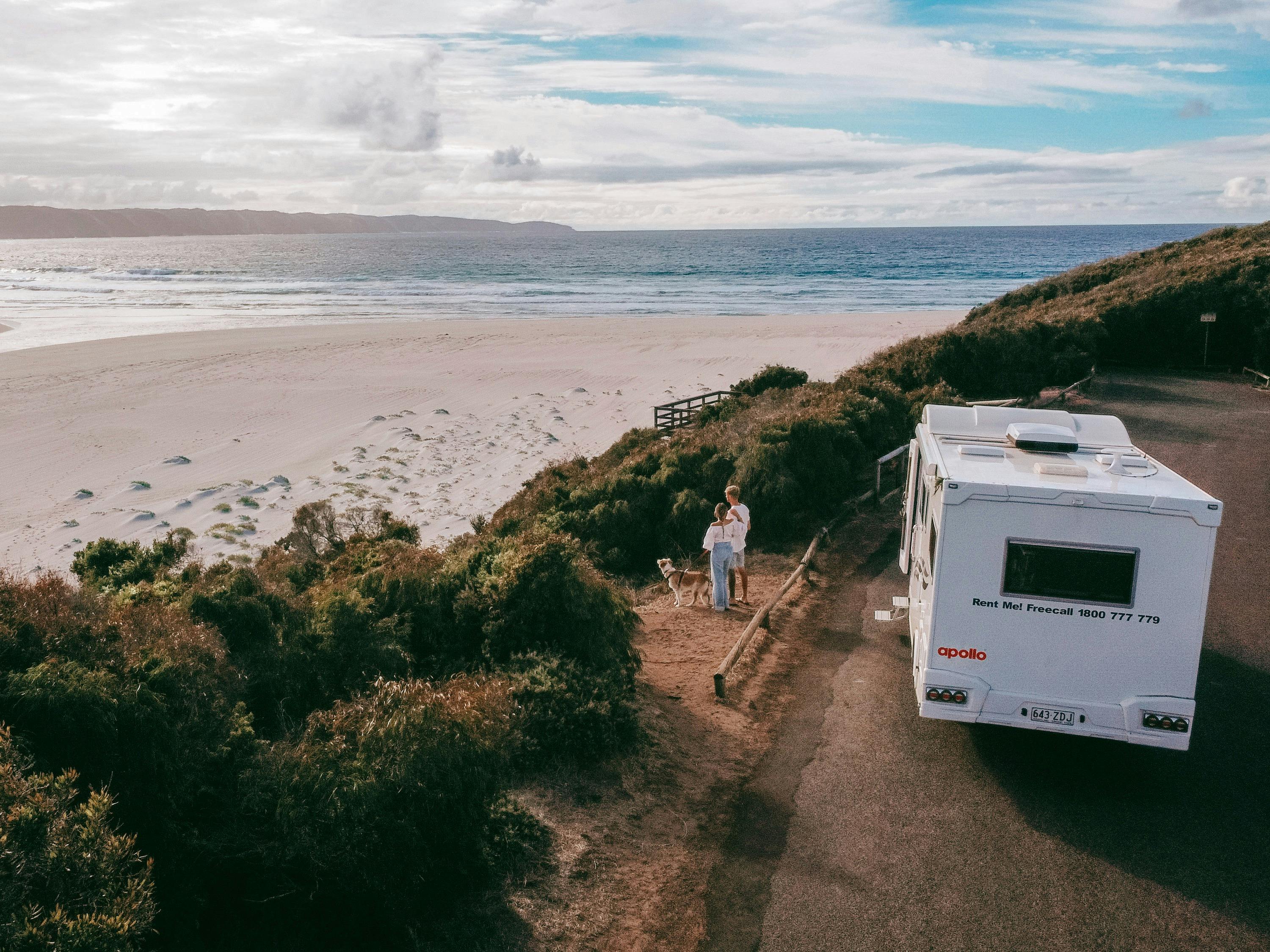 A young couple and their dog park their motorhome near the ocean to walk along the beach
