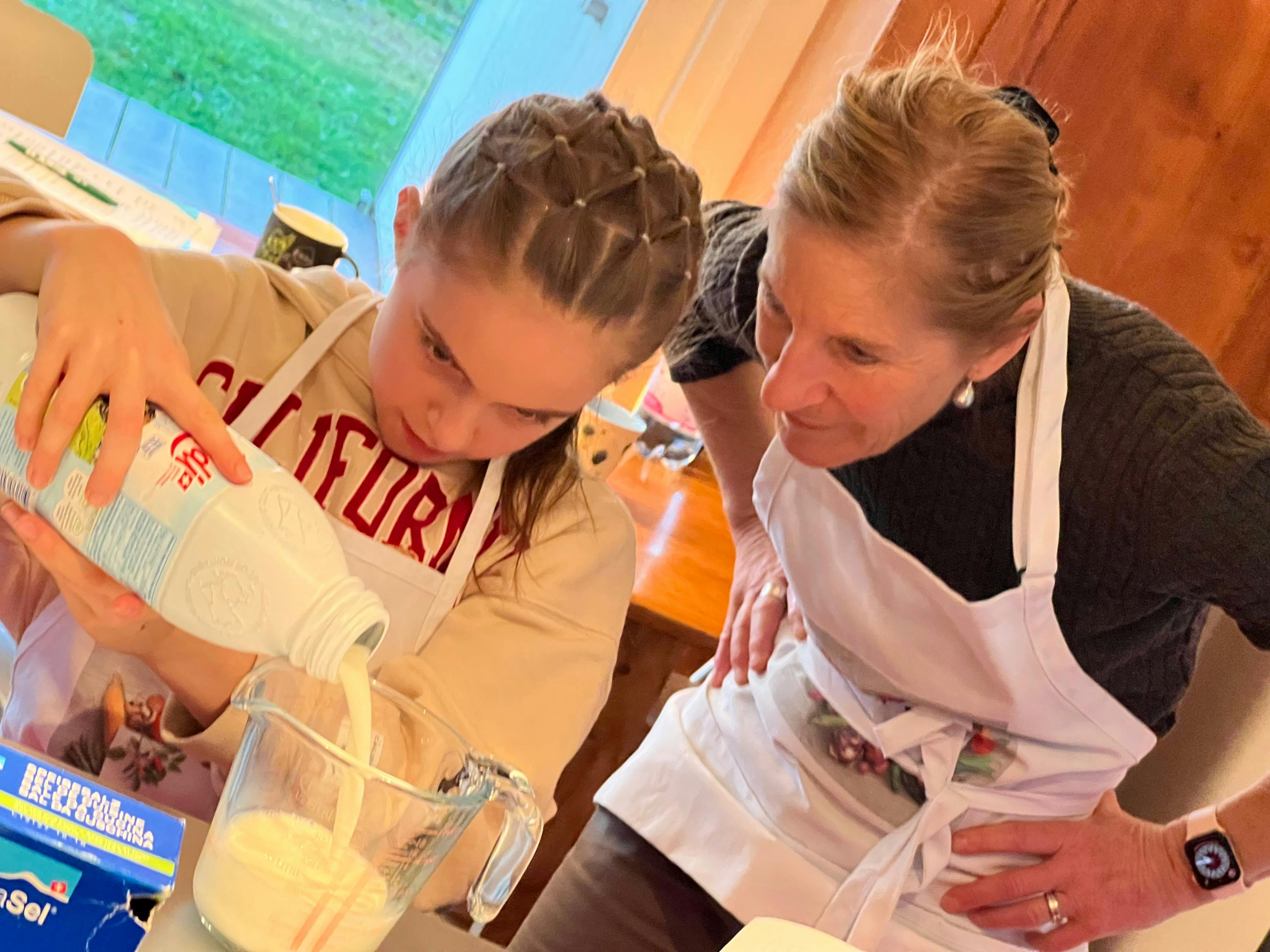 A child pouring milk while Anita Robin leans beside her to offer guidance