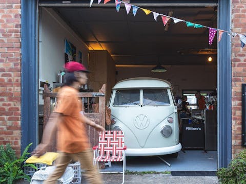 Retro VW van in café garage with bunting, bar setup, and person walking past.