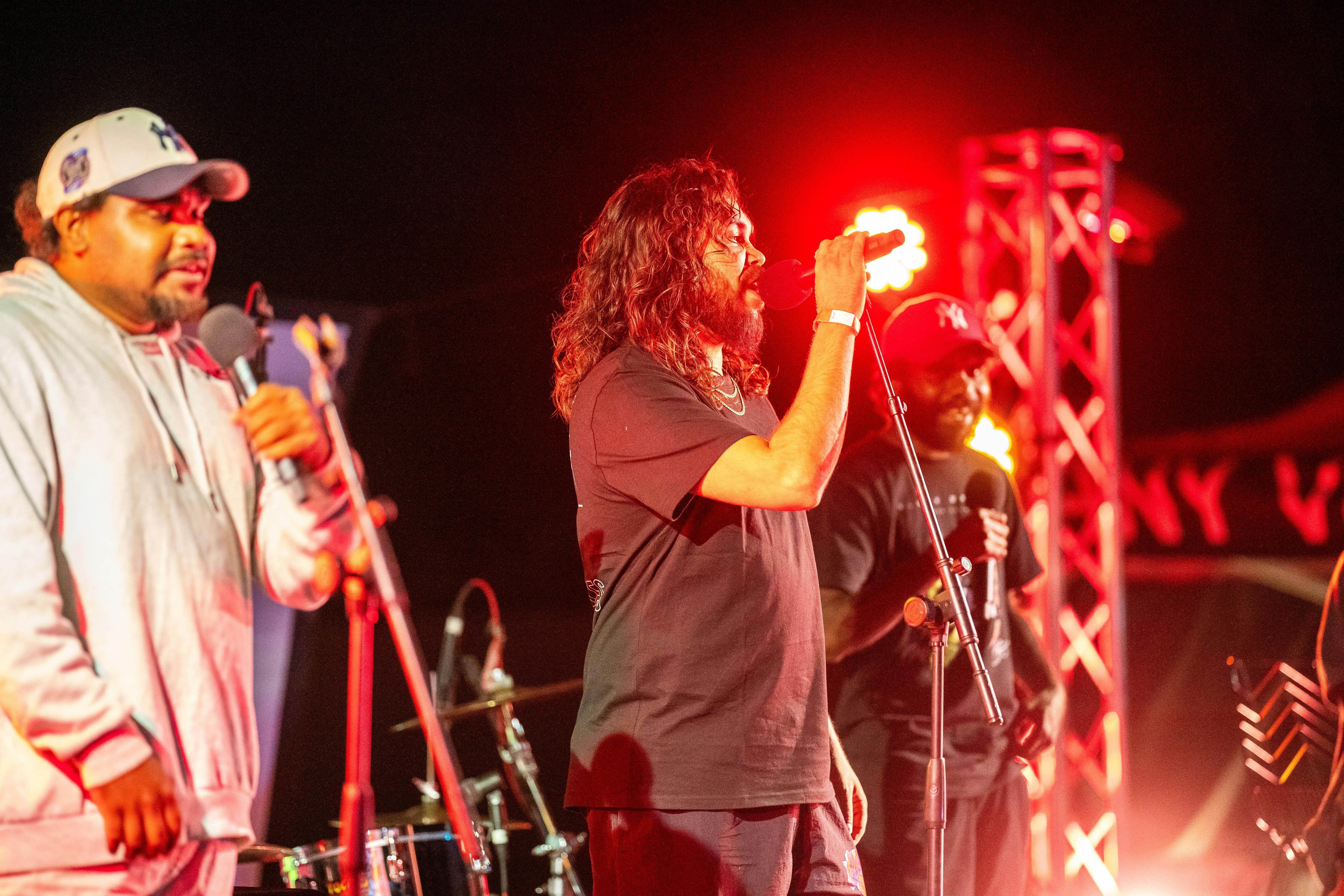 Three male performers onstage, center performer with mic in hand