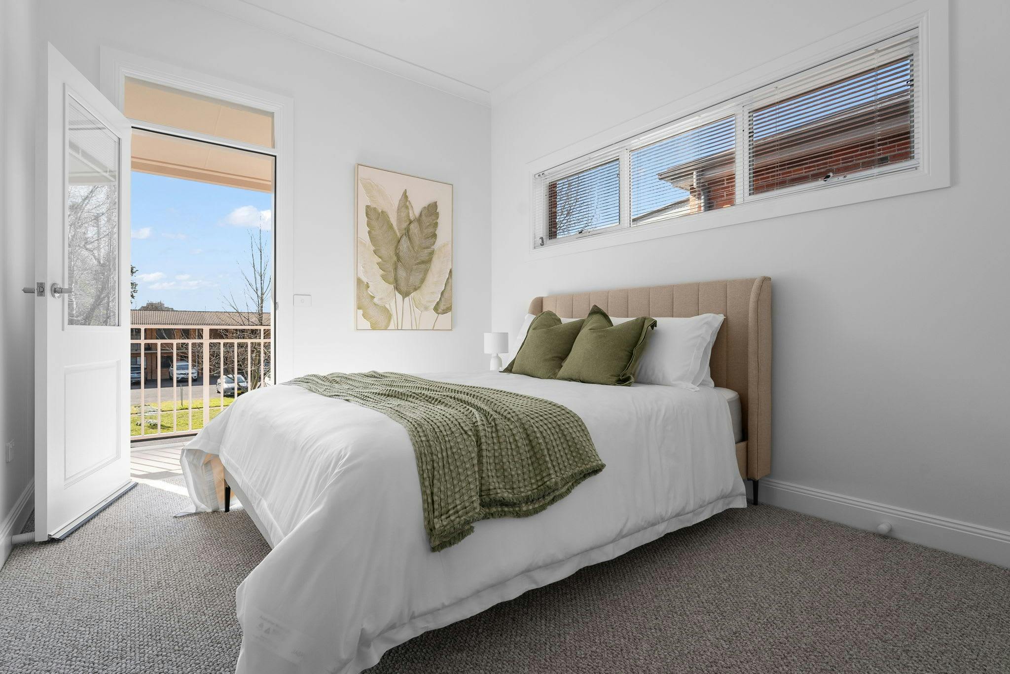 Large queen bed with an artwork on the wall with a window above the bed and door to balcony