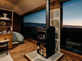 A wood burner stove set against a stone wall with warm dusk views