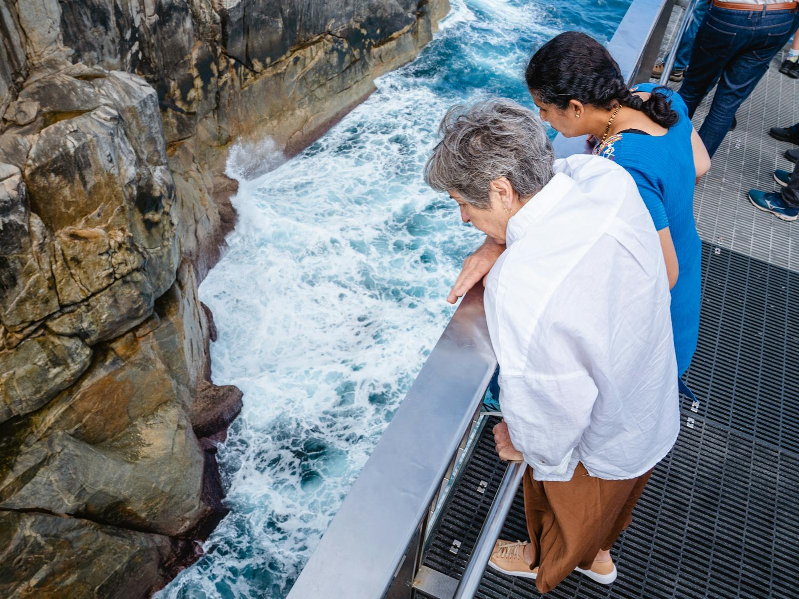 looking down on two women looking into The Gap where water crashes against granite walls
