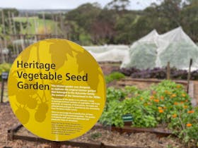 Sign for Heritage Vegetable Seed Garden with garden beds in background