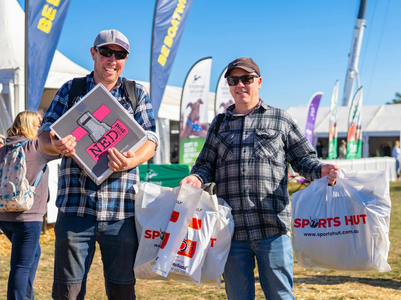 Two men proudly hold their Agfest 2024 purchases, smiling in front of exhibitor stalls.