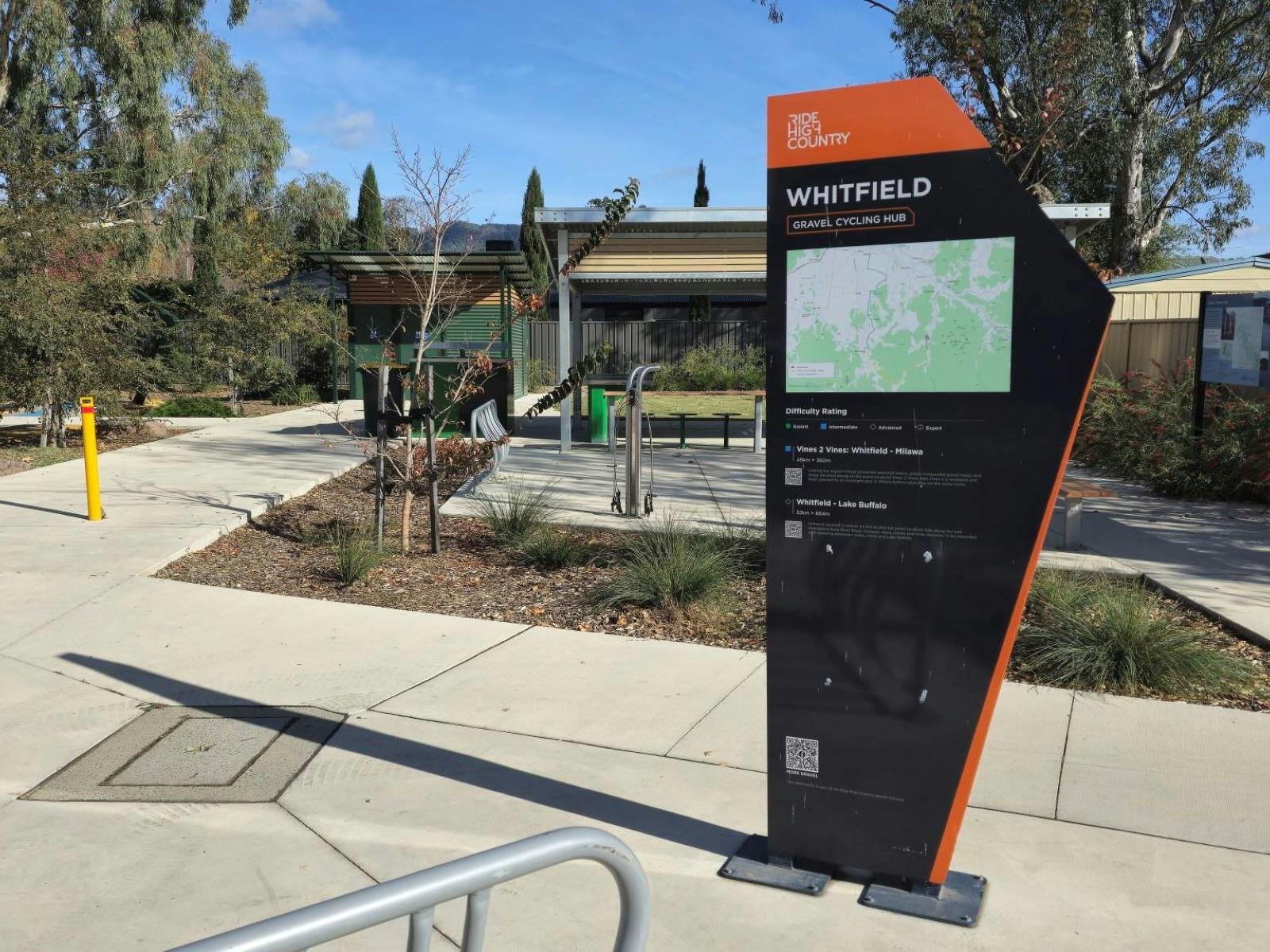 Black and orange sign that says 'Whitfield Gravel Cycling Hub' on a concrete path