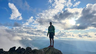 A hiker standing on a rock in the mountains with some clouds behind them.