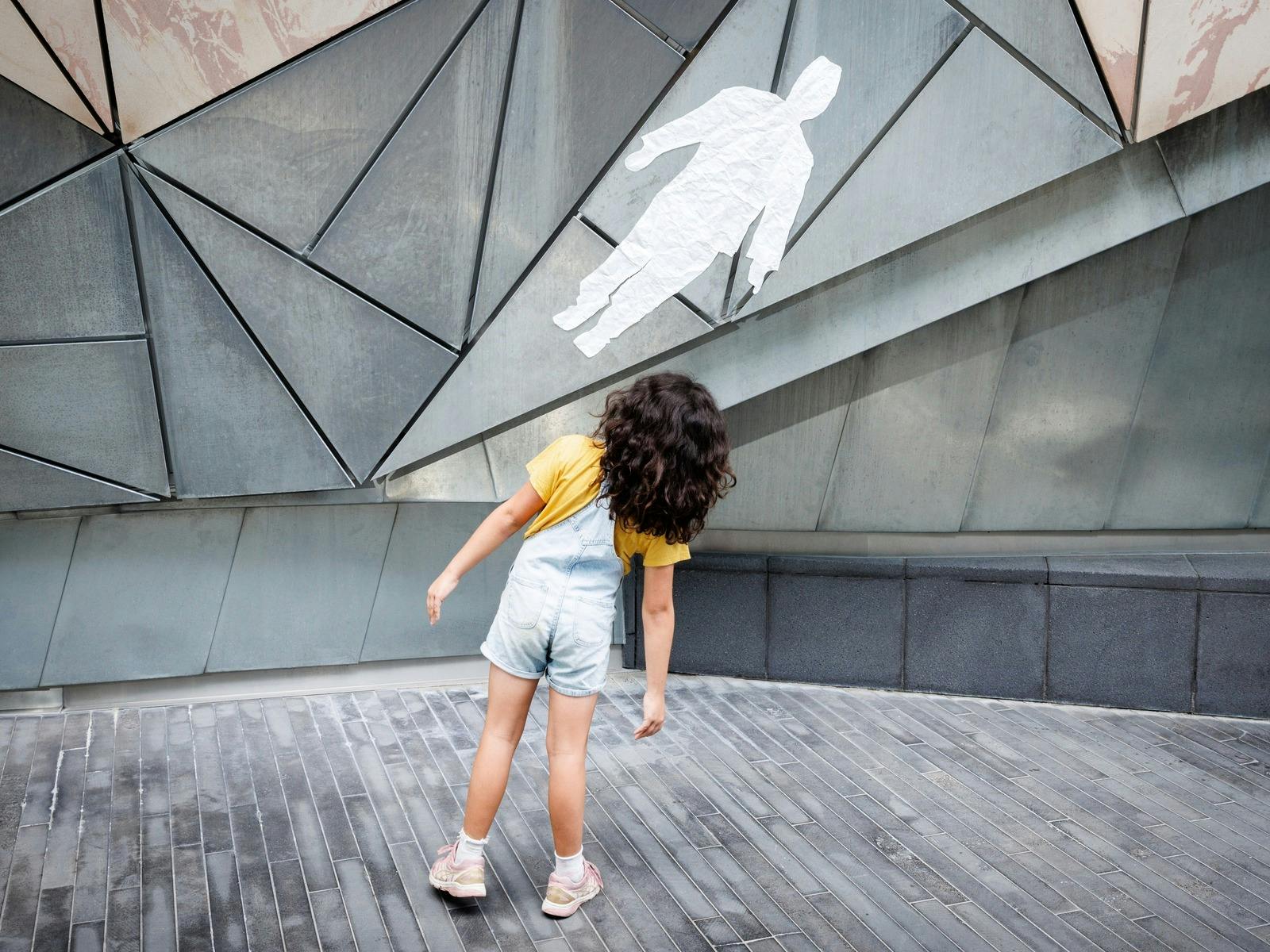 A child leans to the side while imitating a silhouette pasted on the Fed Square wall