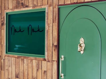 Arched green doorway into Nok Nok. Adorned with a gold door knocker in the shape of a hand