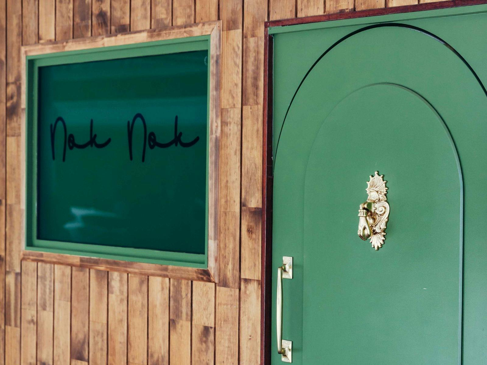 Arched green doorway into Nok Nok. Adorned with a gold door knocker in the shape of a hand Arched green doorway into Nok Nok. Adorned with a gold door knocker in the shape of a hand