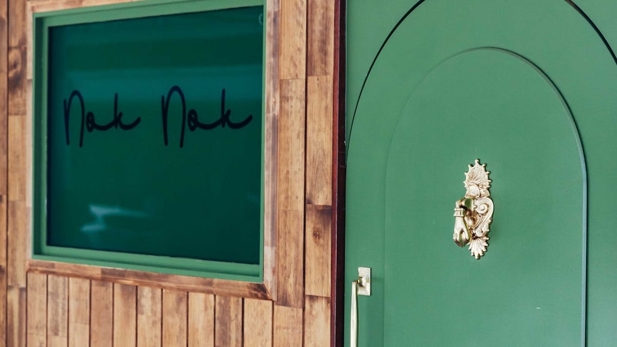 Arched green doorway into Nok Nok. Adorned with a gold door knocker in the shape of a hand
