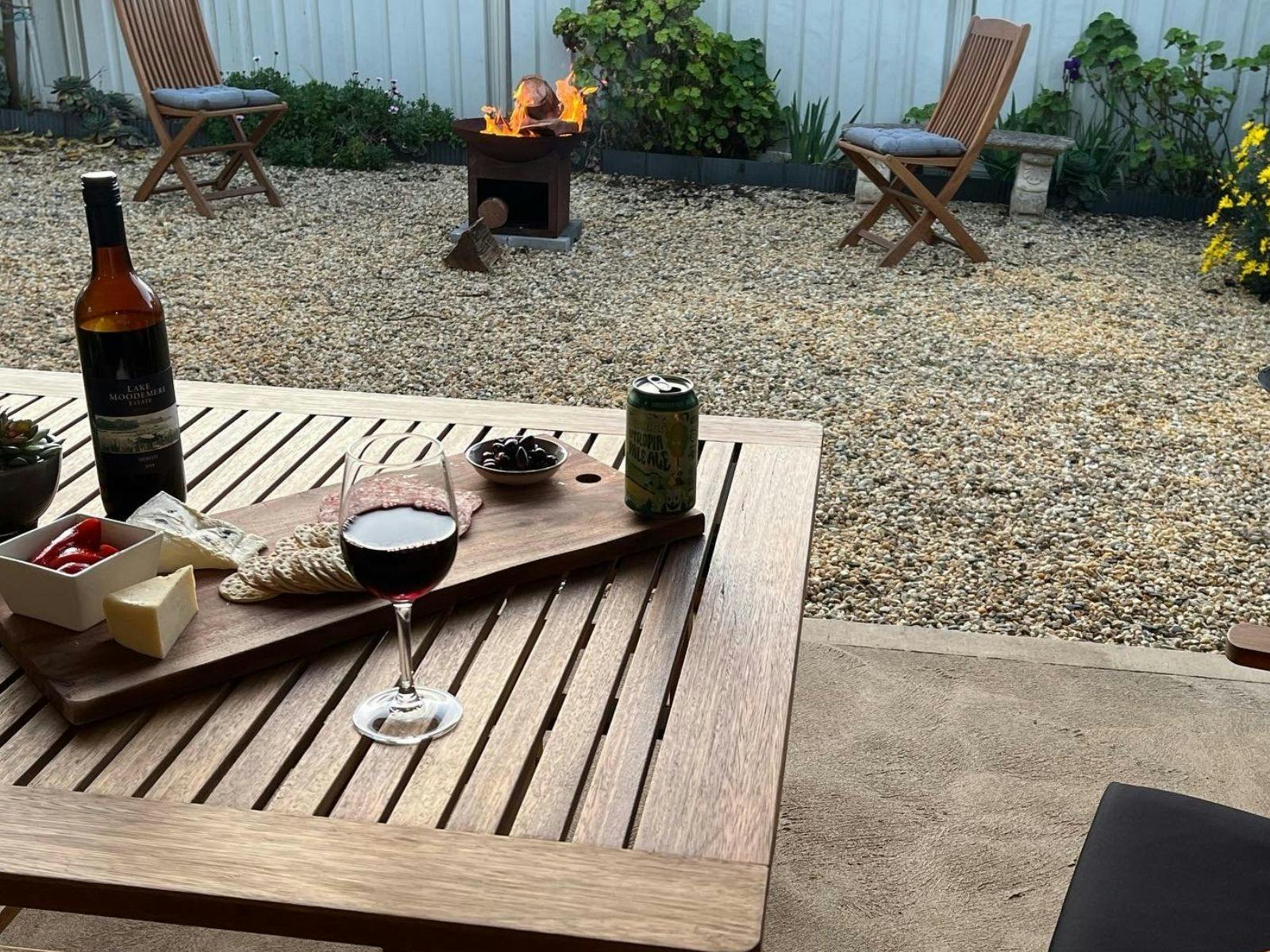 A wooden outdoor setting with wine and grazing platter. In the background a fire pit crackles away.
