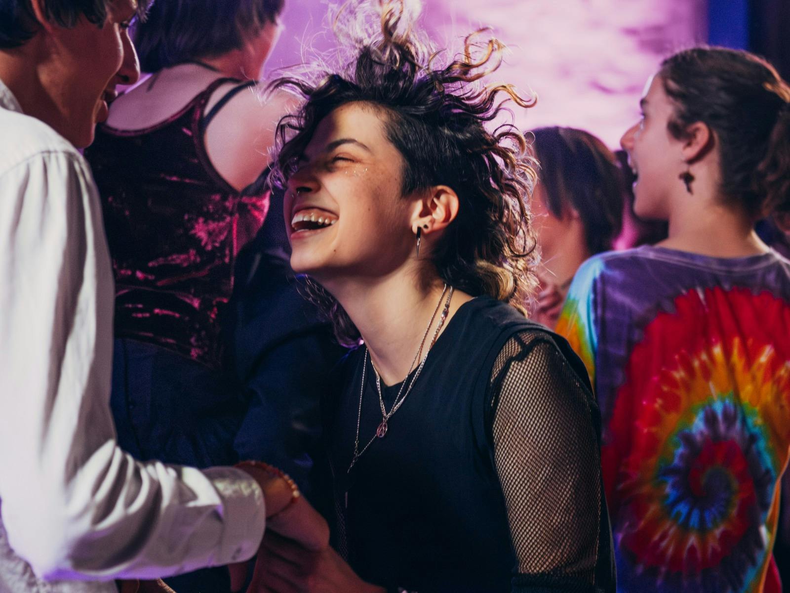 A group of people dancing and laughing under a purple light.