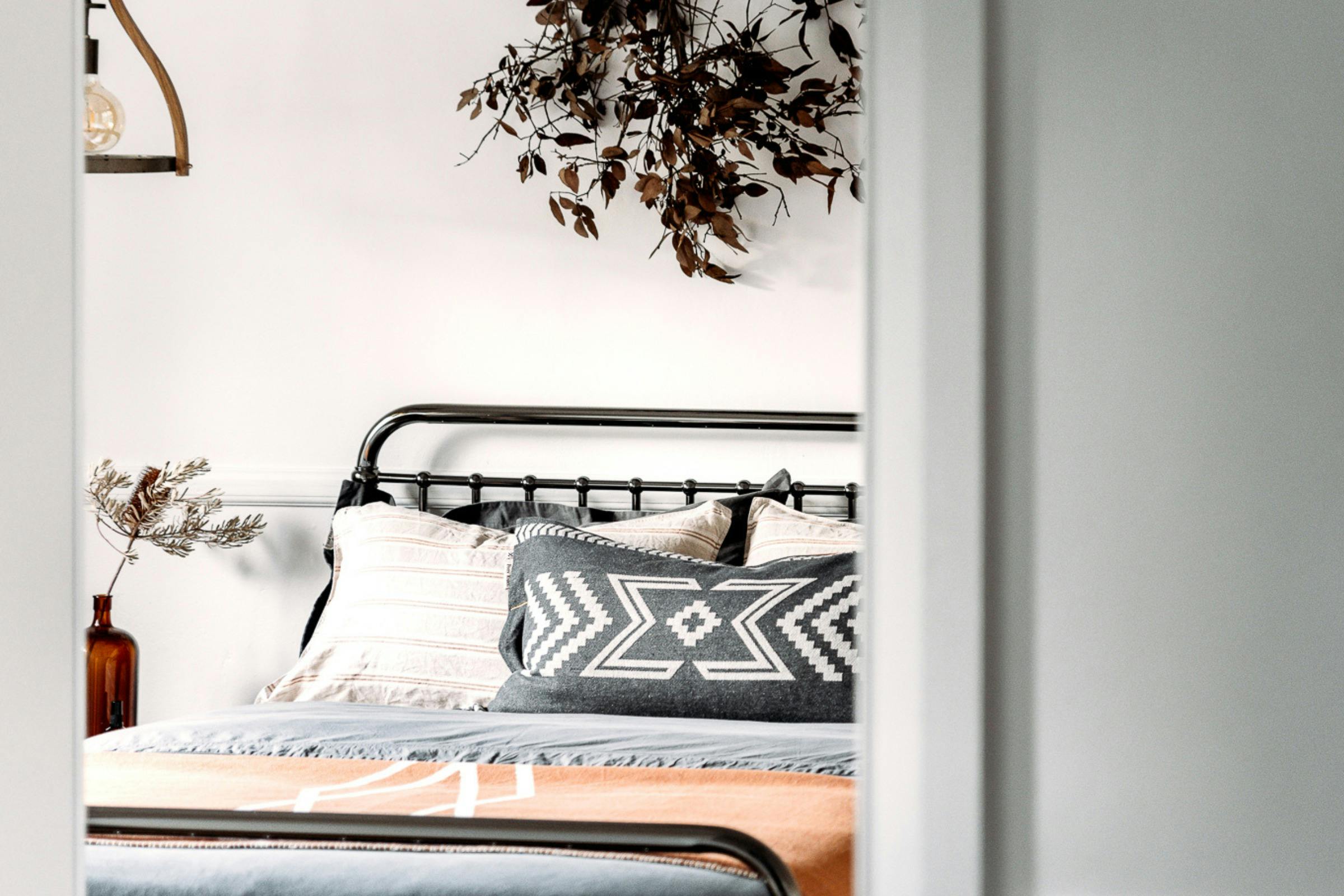 Black metal bed frame with layered patterned cushions and soft bedding.