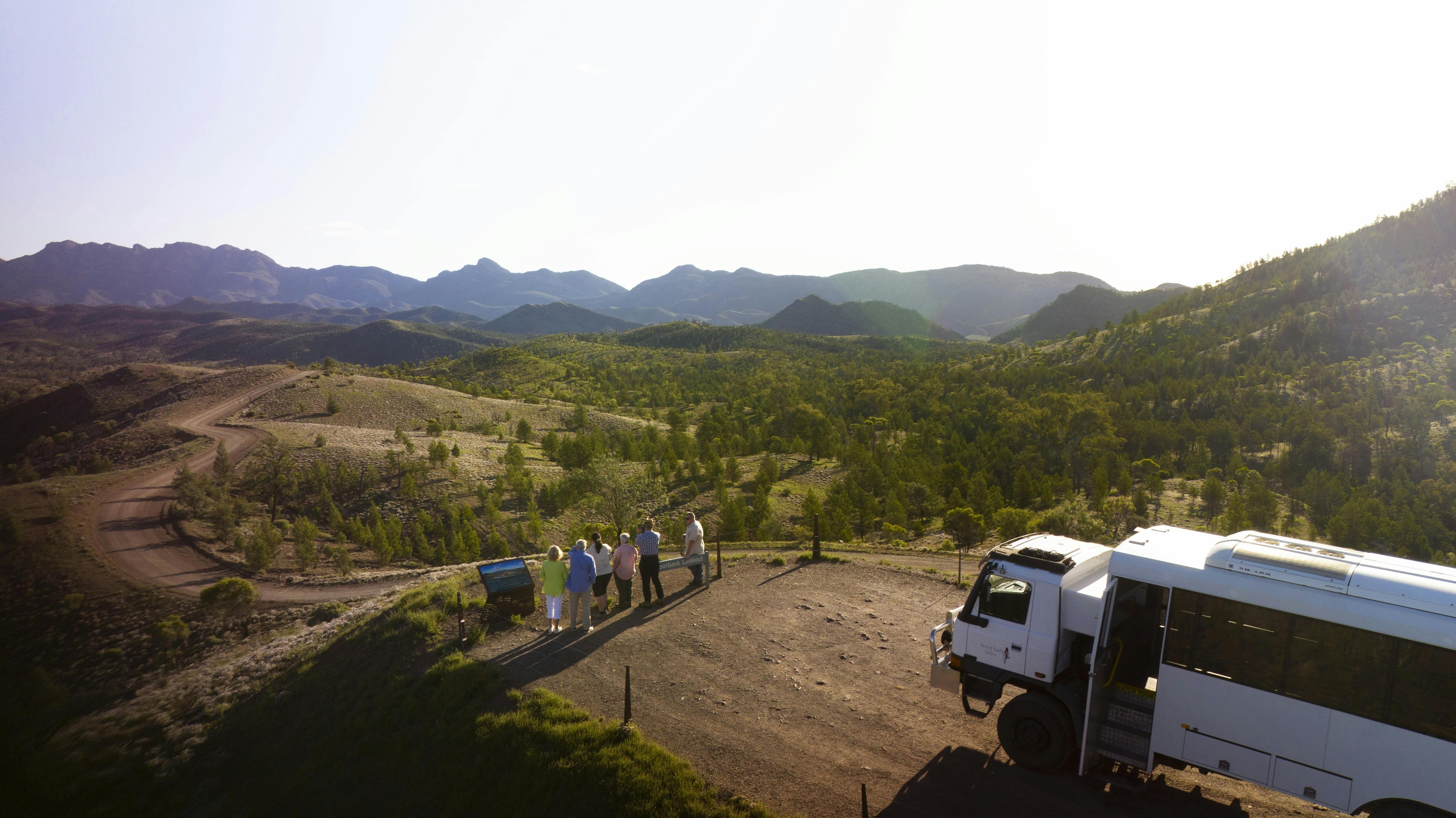 Group of people at a mountain lookout with tour coach behind them