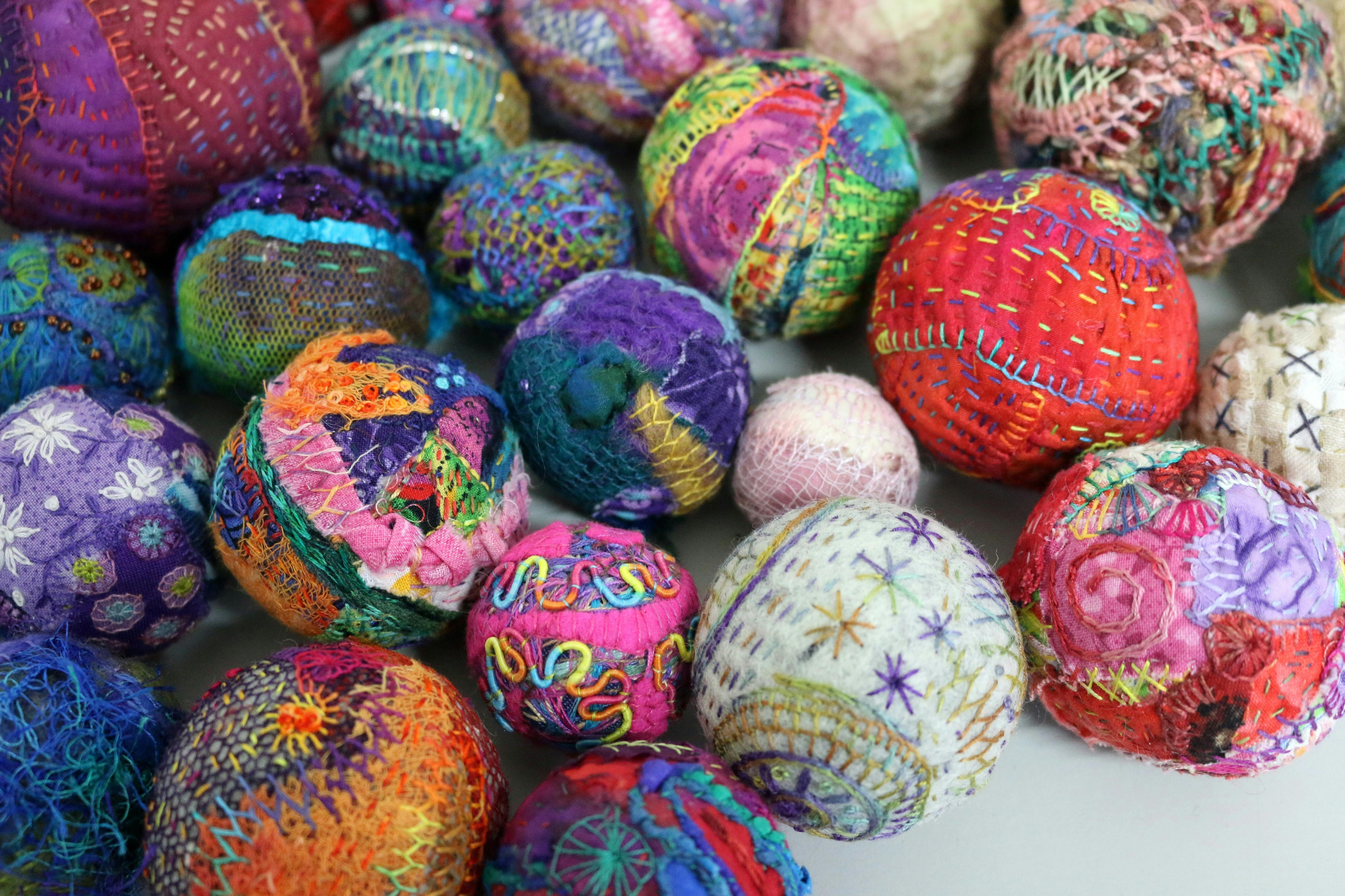 A close-up collection of handmade fabric spheres, covered in embroidery.