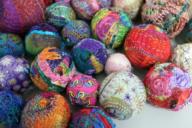 A close-up collection of handmade fabric spheres, covered in embroidery.