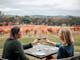 Two women at a table with red wine in glasses overlooking autumnal vines