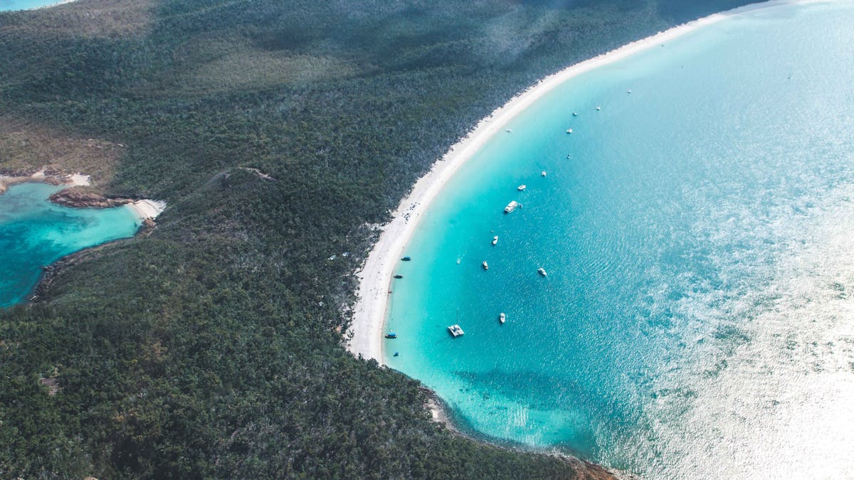 Aerial view of the long stretch of Whitehaven Beach surrounded by blue waters and national park