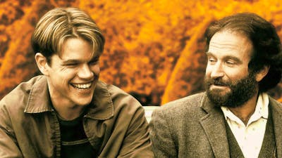 Two men sit next to each other, man on left laughing