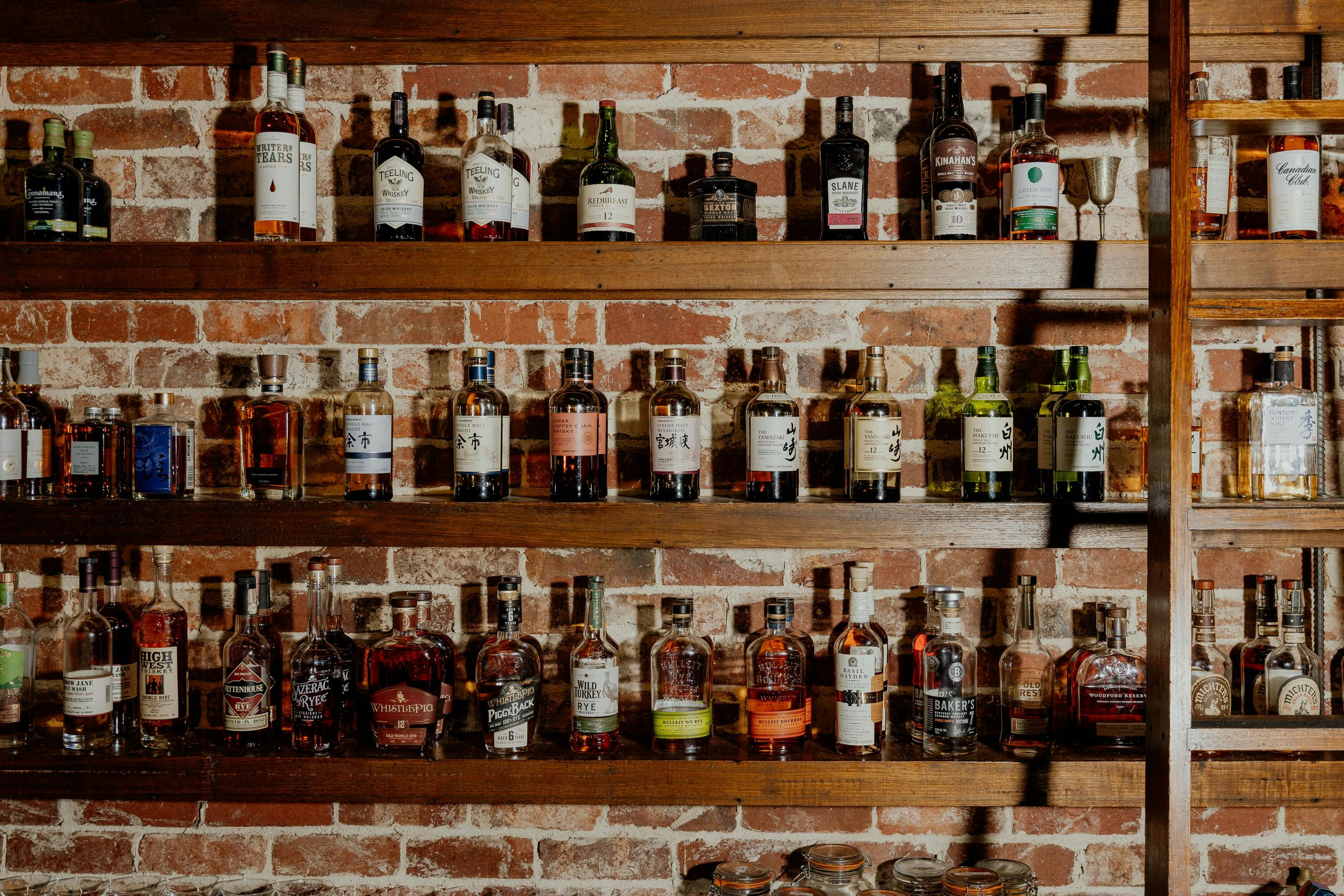 Dark wood shelves are topped with several hundered whisky brands on display a ladder is on the right