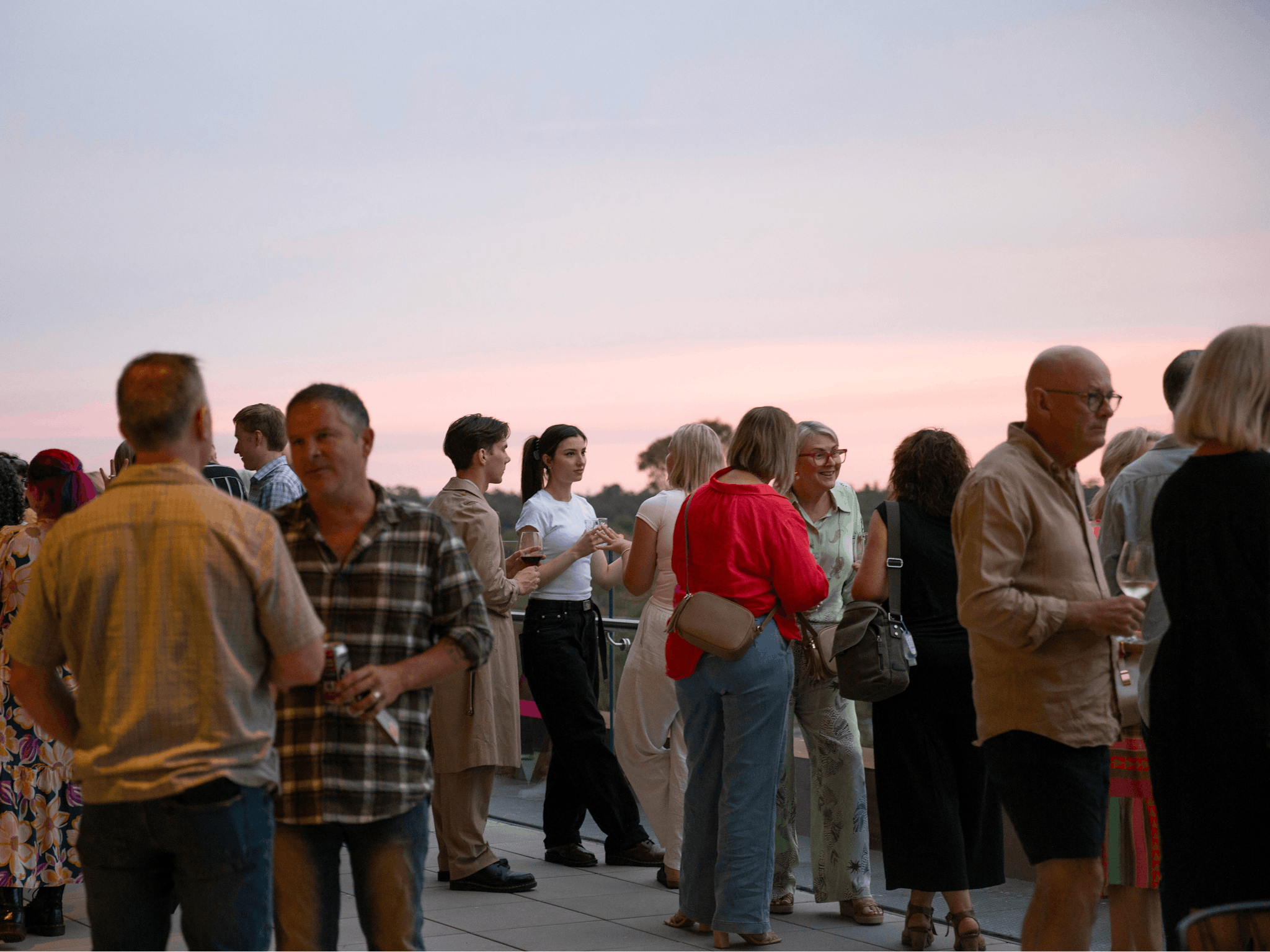People standing on an outdoor terrace at dusk, drinking wine