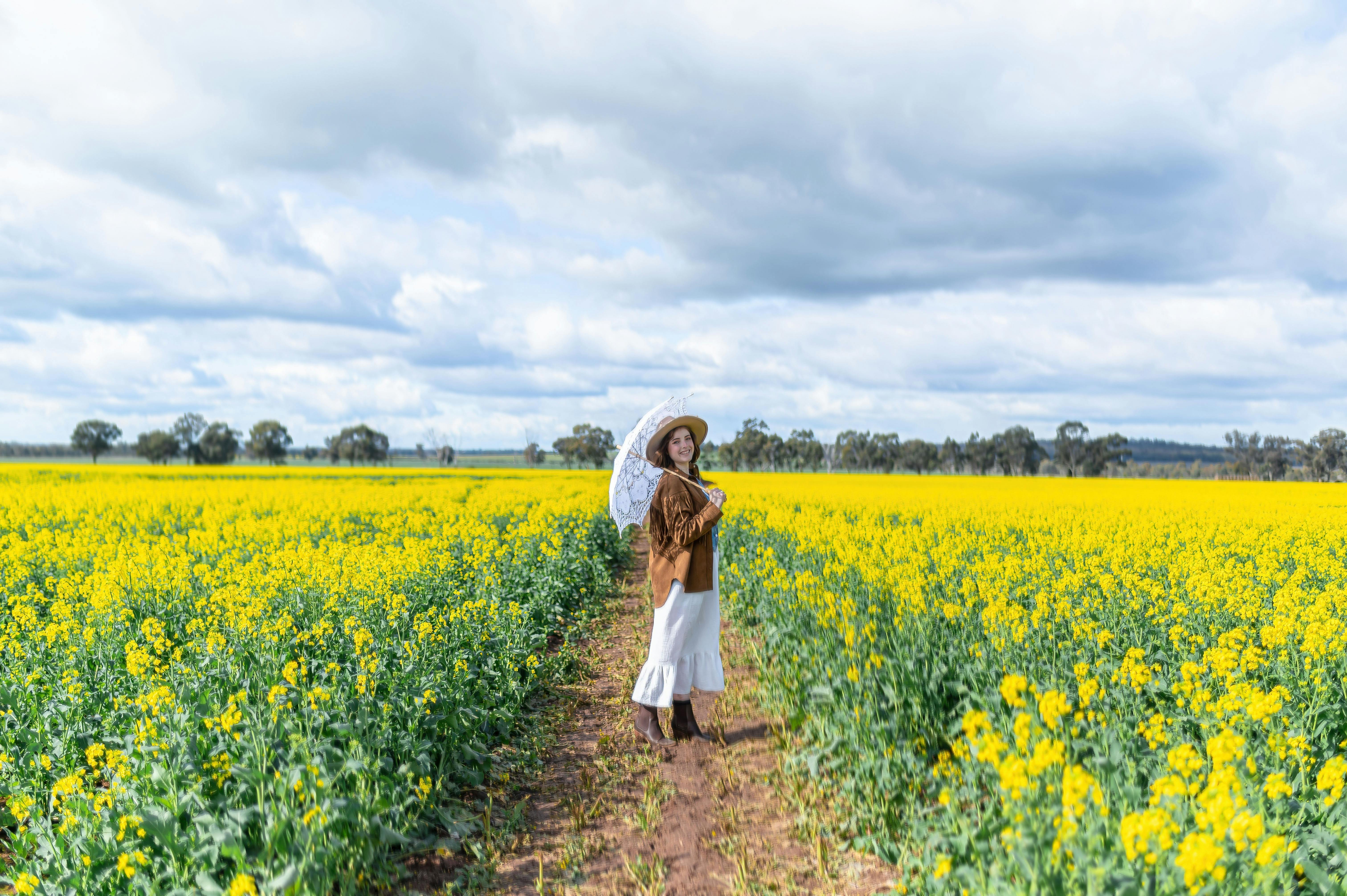 A girl standing in the canola field holding up an umbrella