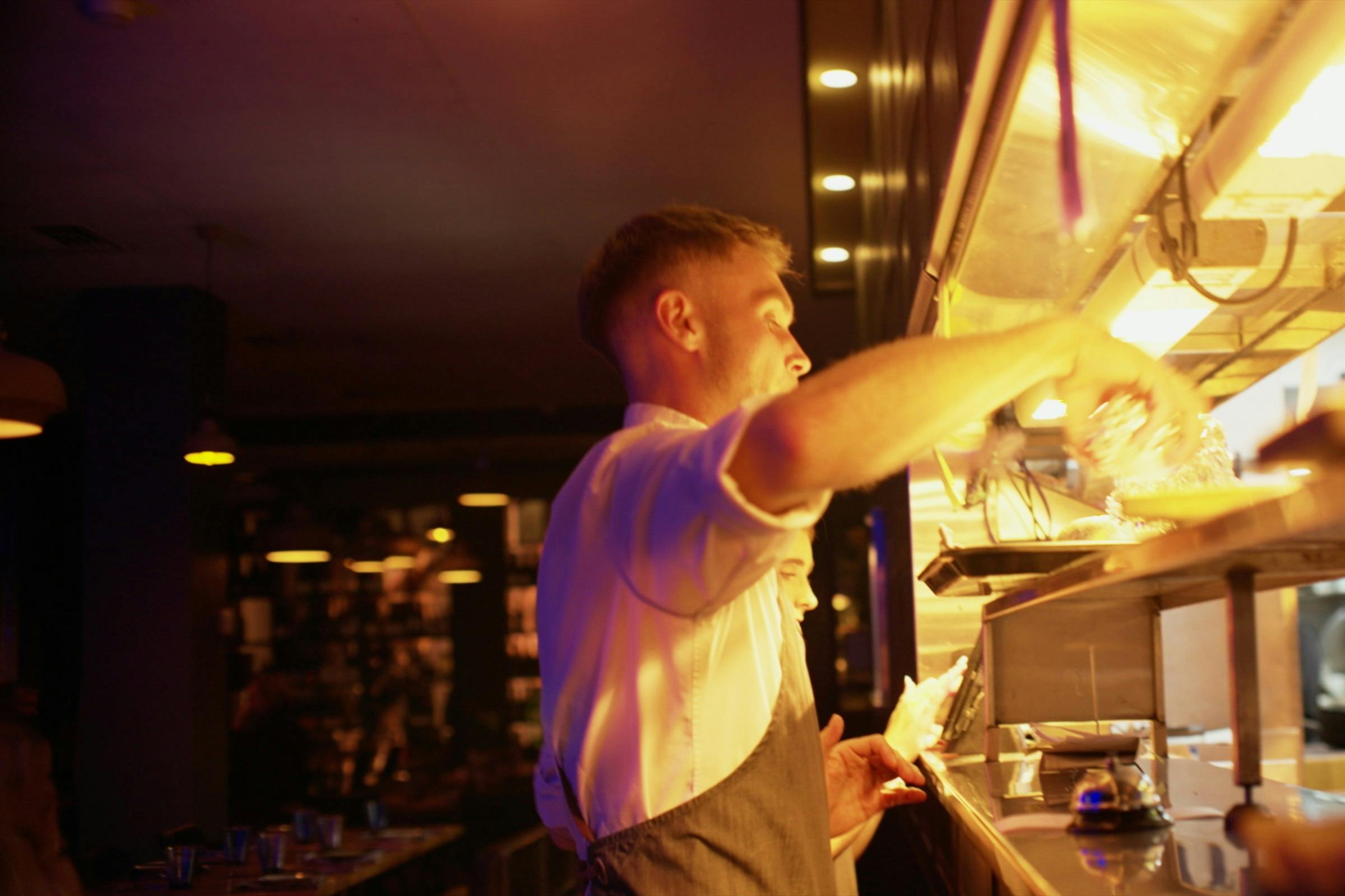 Waiter collecting dishes from the kitchen pass at Mudbar Restaurant in Launceston