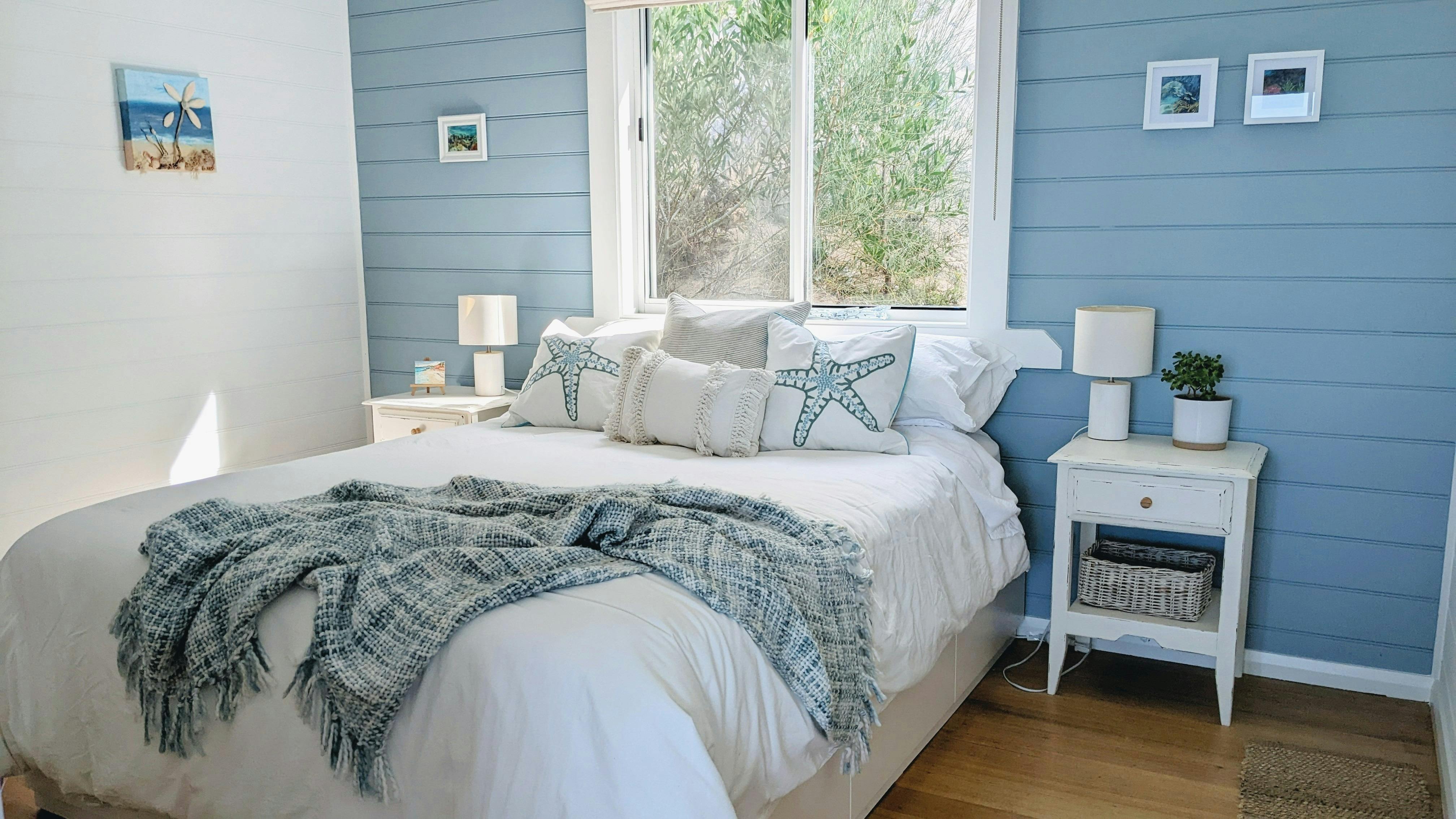 A queen-size bed in a seaside themed bedroom with blue wall, white doona, side tables and throw
