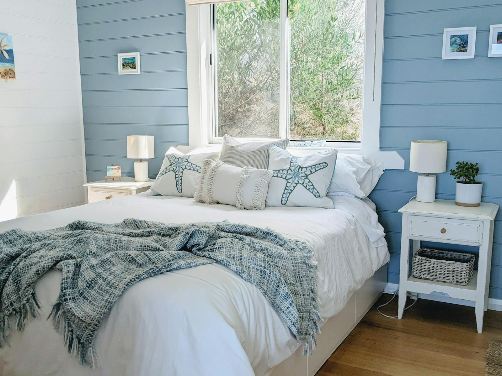 A queen-size bed in a seaside themed bedroom with blue wall, white doona, side tables and throw