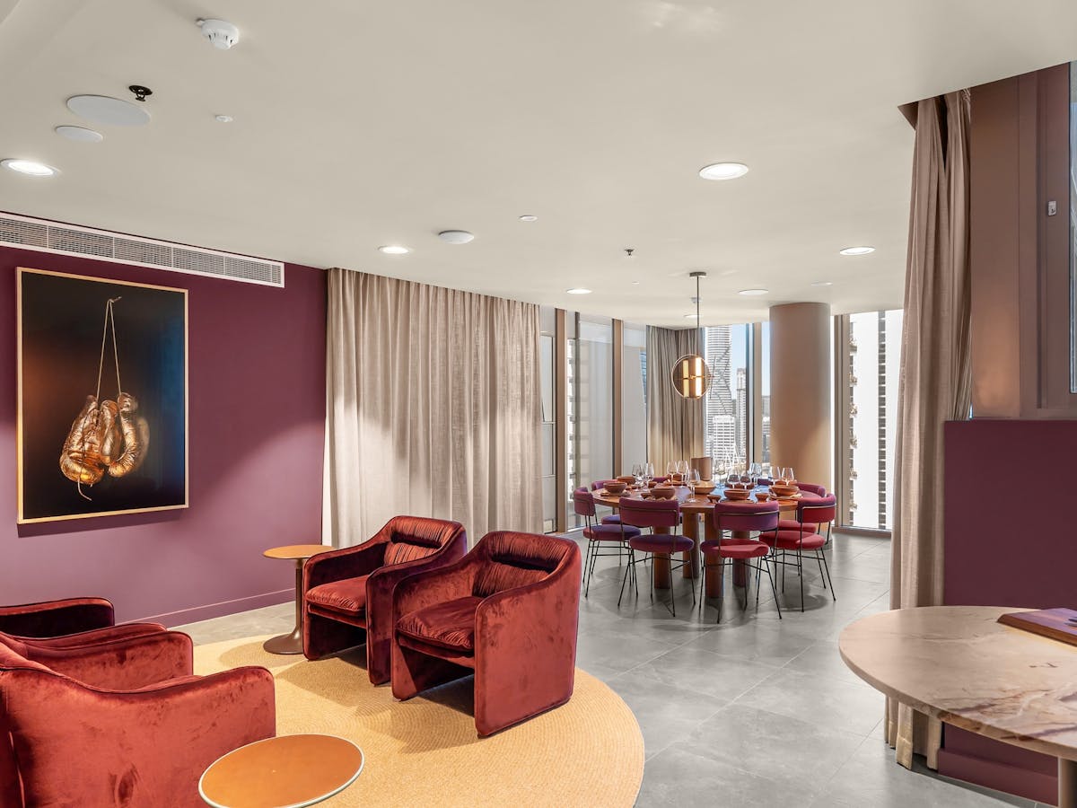Large 8-seater dining table with burgundy chairs and gold accents beside 4 red armchairs.