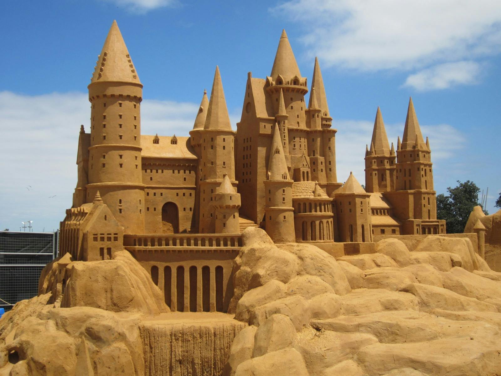 Sand sculpture of a grand castle with tall spires under a blue sky.