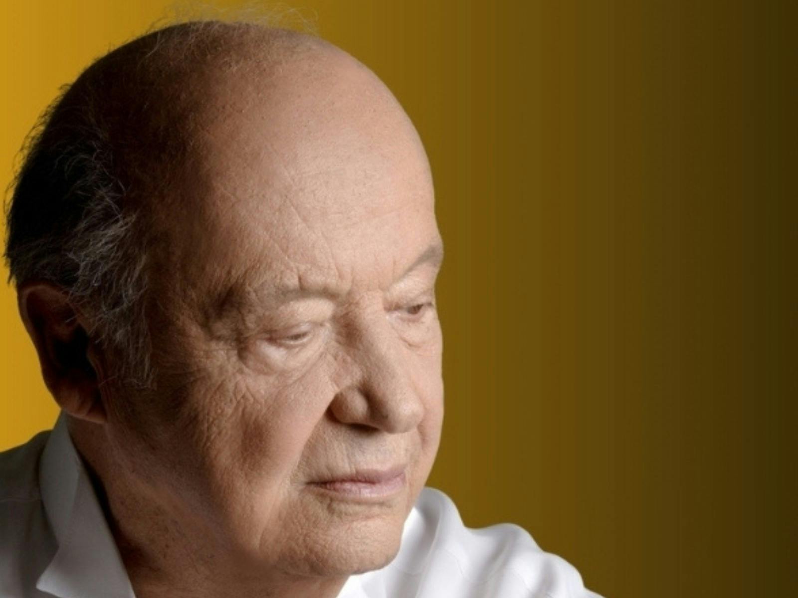 Man with his face tilting right, away from the camera. He is looking down and wearing a white shirt,