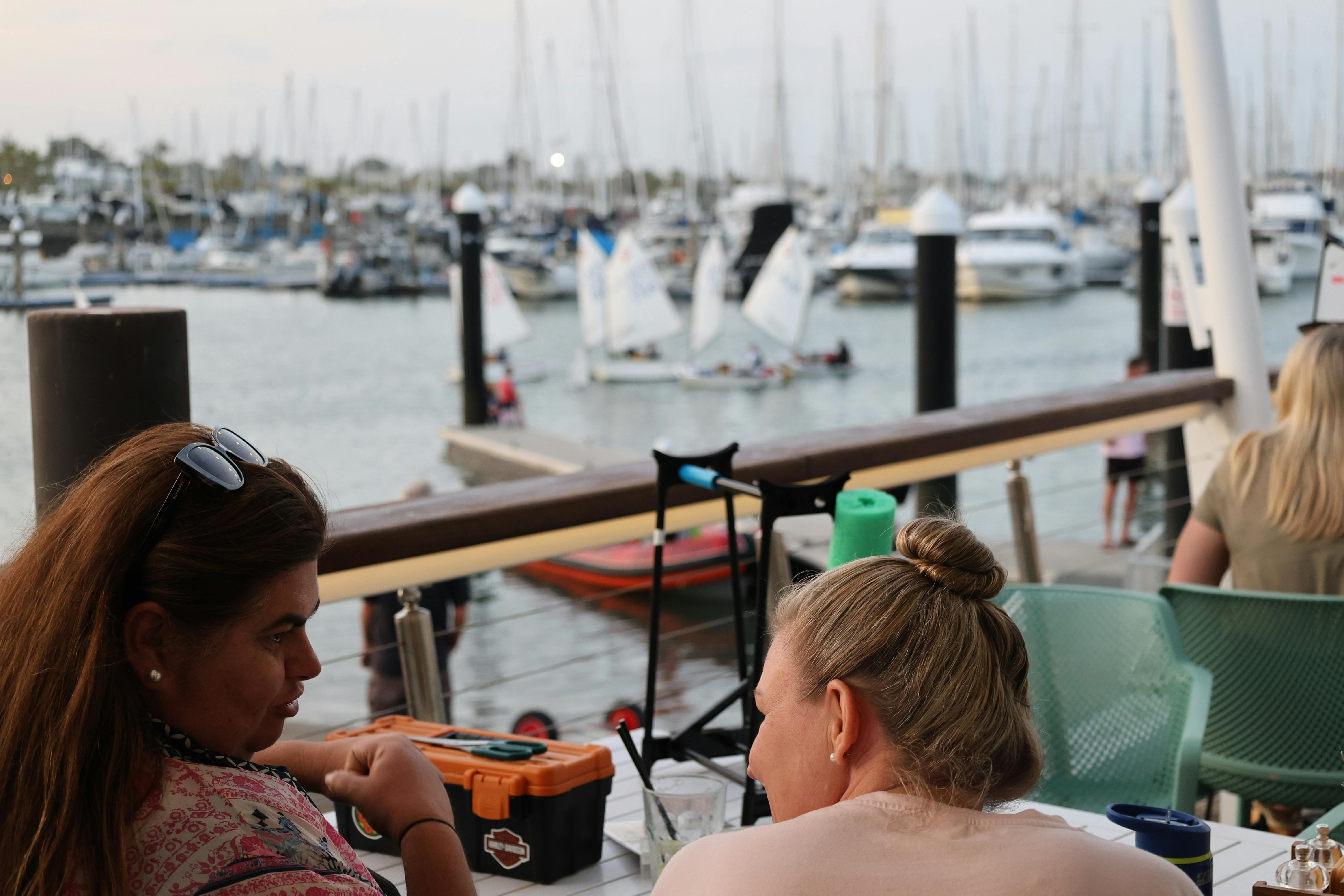 People sitting on a boardwalk watching boats go by
