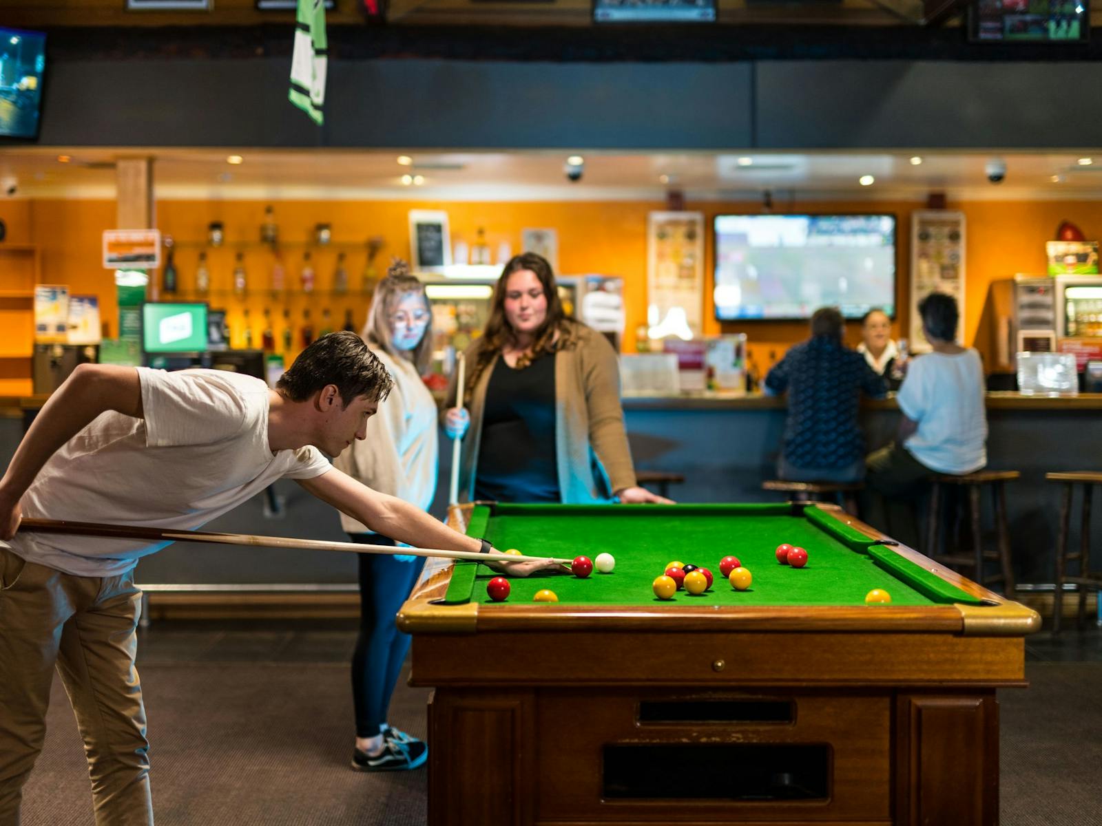 Young man lining up a shot at a pool table in Millers Sports Bar with others watching on