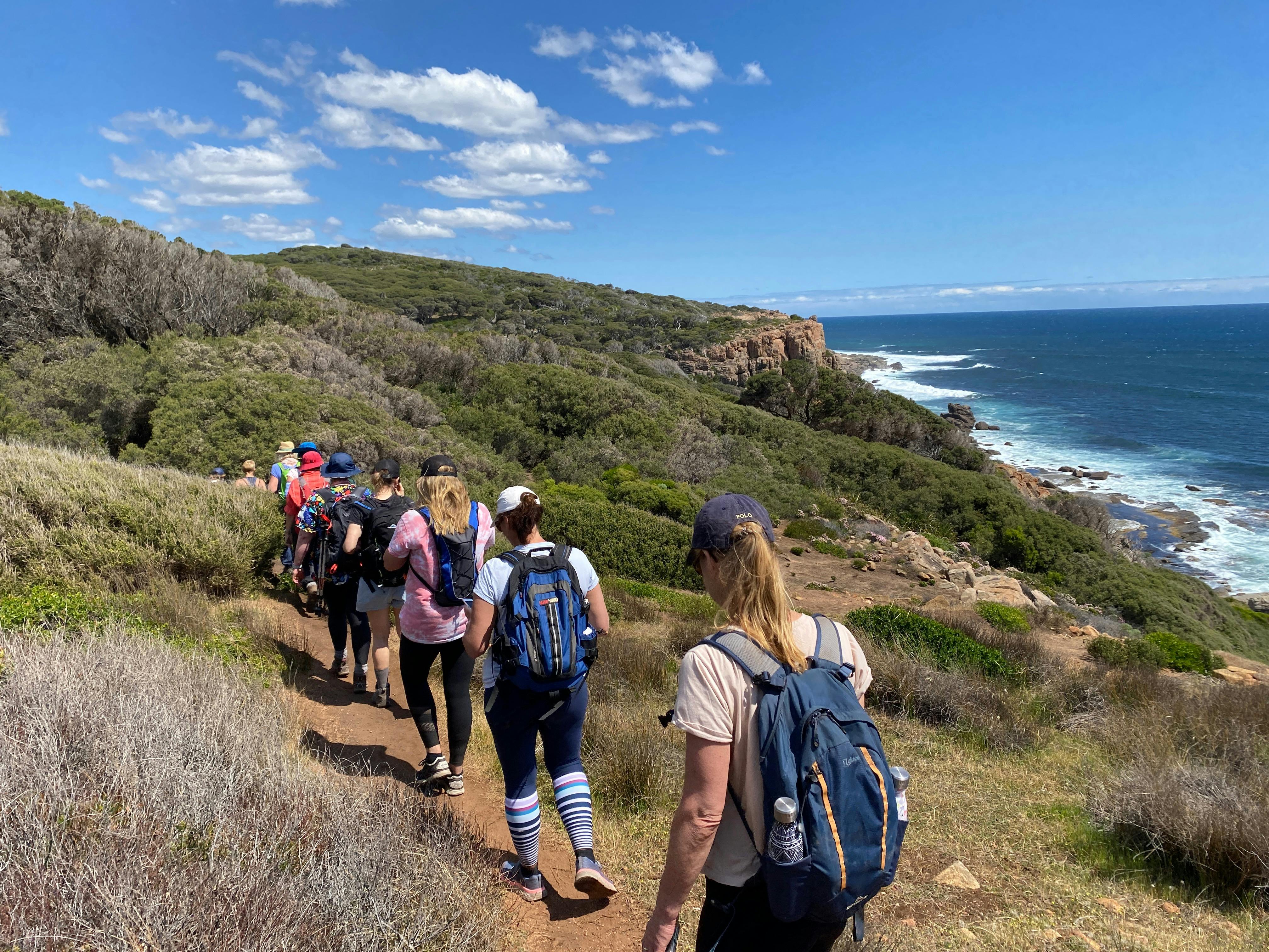 Women walking along a narrow path with the spectacular granite cliffs & ocean in front.