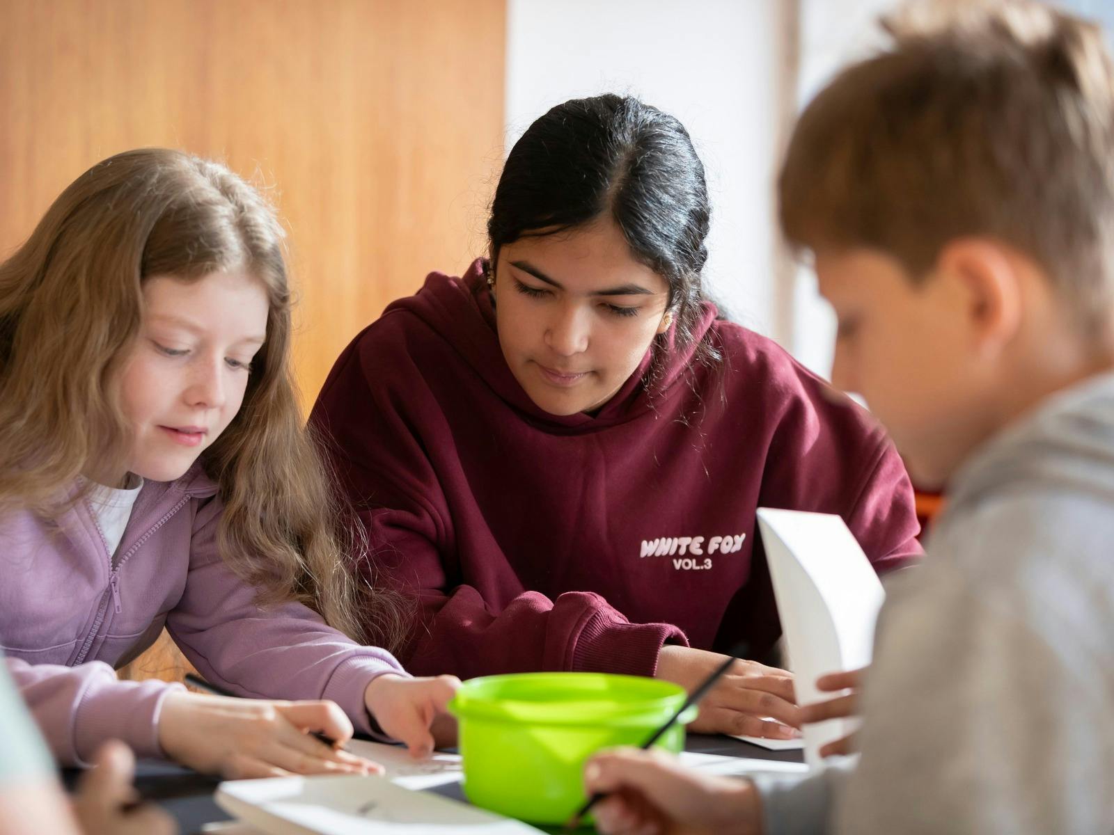 Three students are focused on an art project at a table.