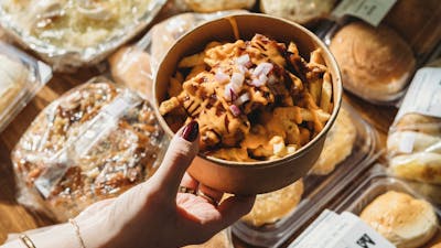 A hand holding a bowl of lechon loaded fries topped with cheese and onions, surrounded by assorted F