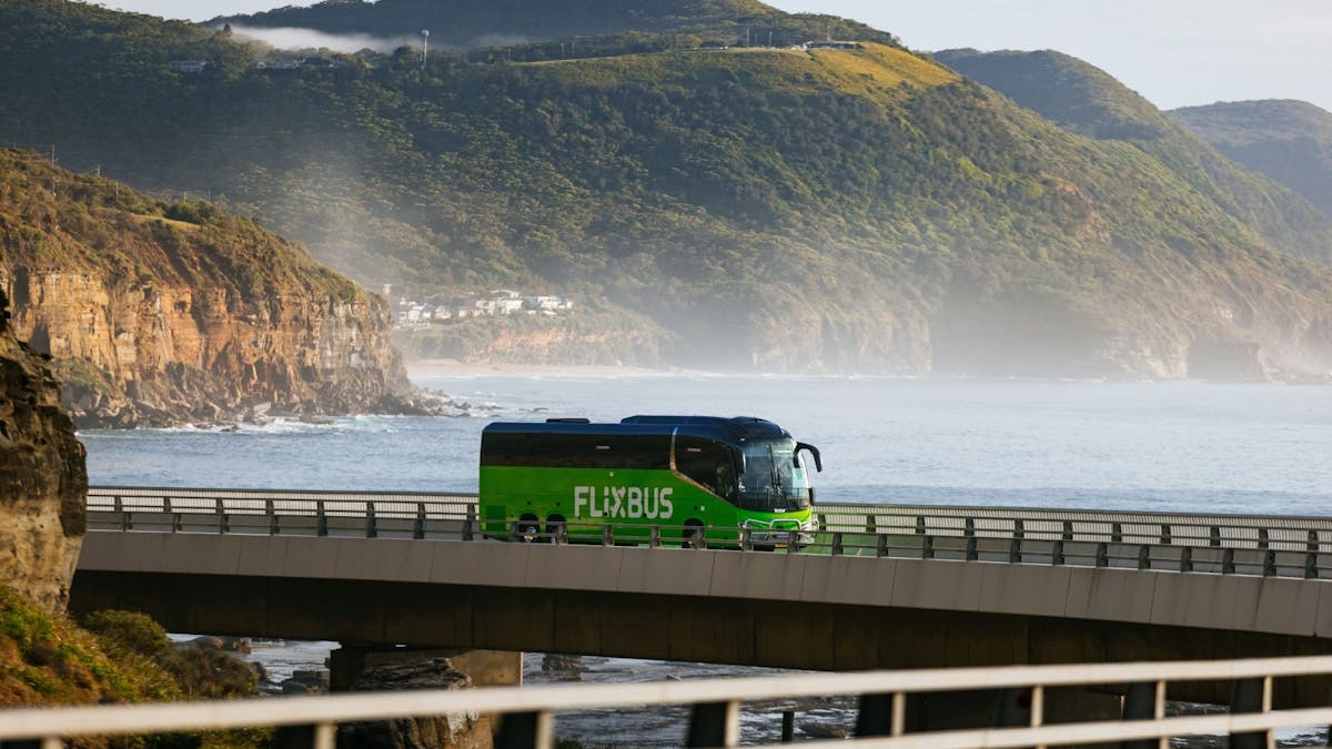 A green flixbus driving on a bridge with sea and mountains in the background. A green flixbus driving on a bridge with sea and mountains in the background.