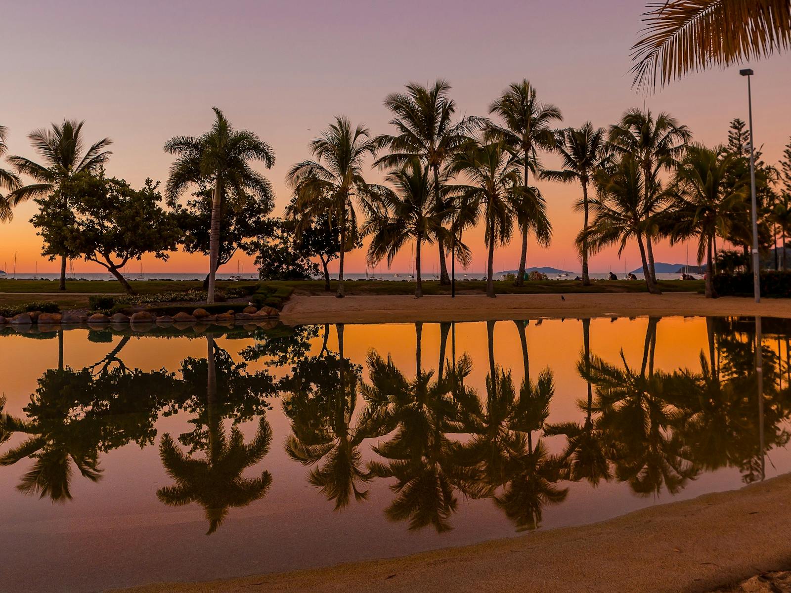 Palm trees and reflections on the water in the lagoon at sunset with beautiful orange and pink sky