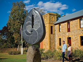 Stone sculpture in front of heritage building with couple walking past in Hahndorf's main street