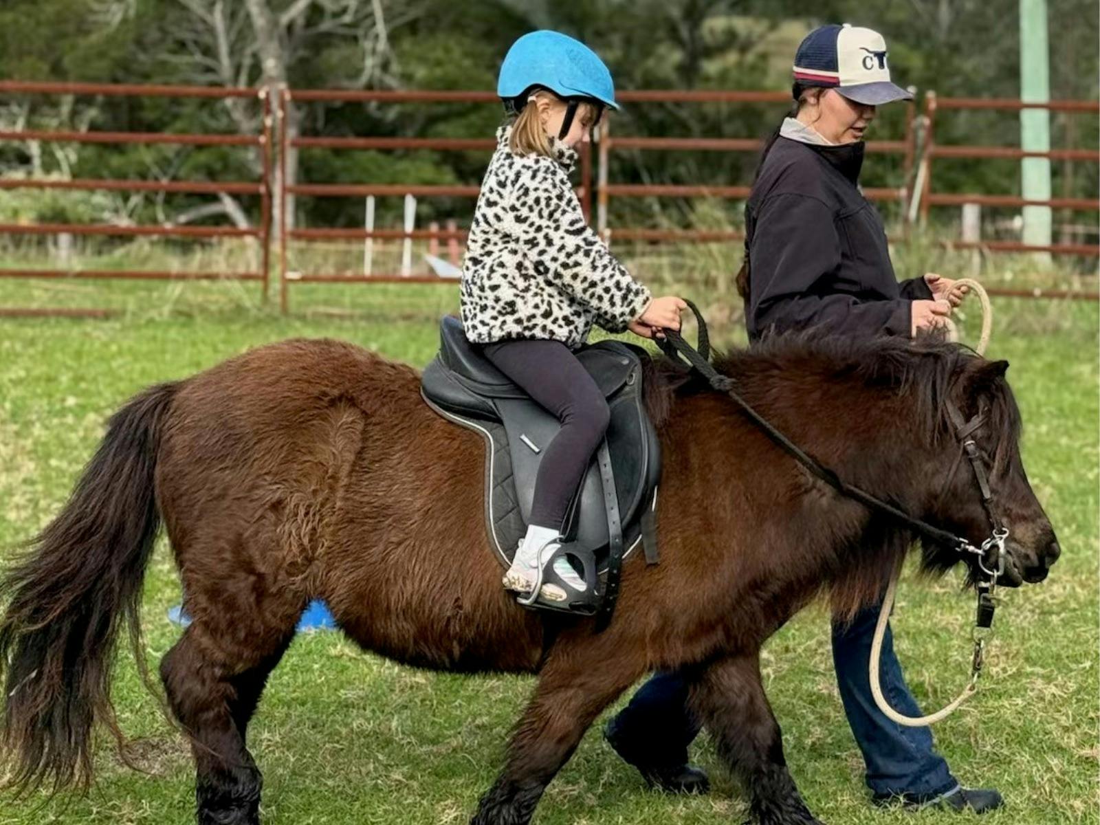 Ausbilder führt kleines Kind auf Sheltlandpony