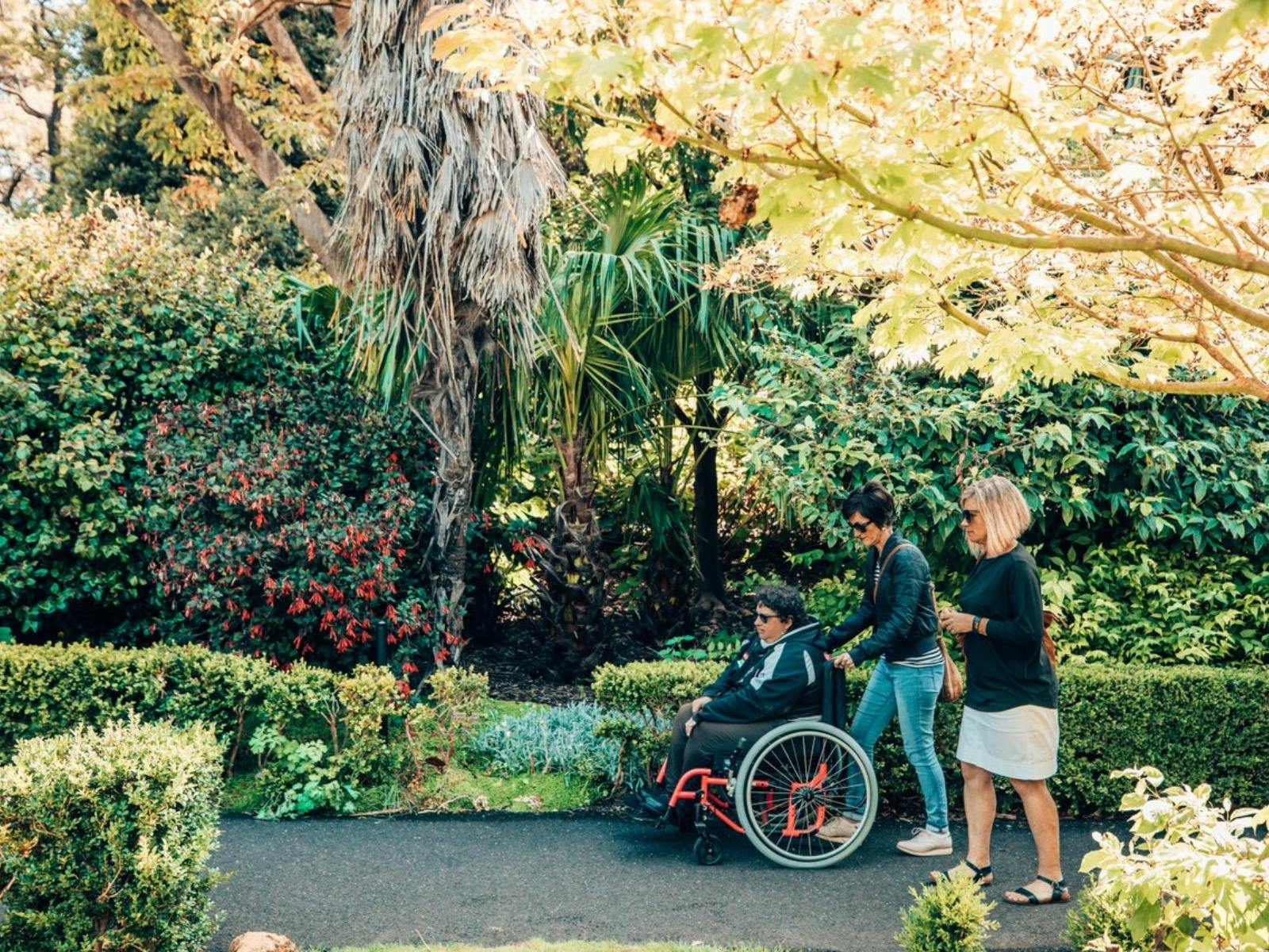 A woman in wheel chair and two women walk beside her discovering the gardens